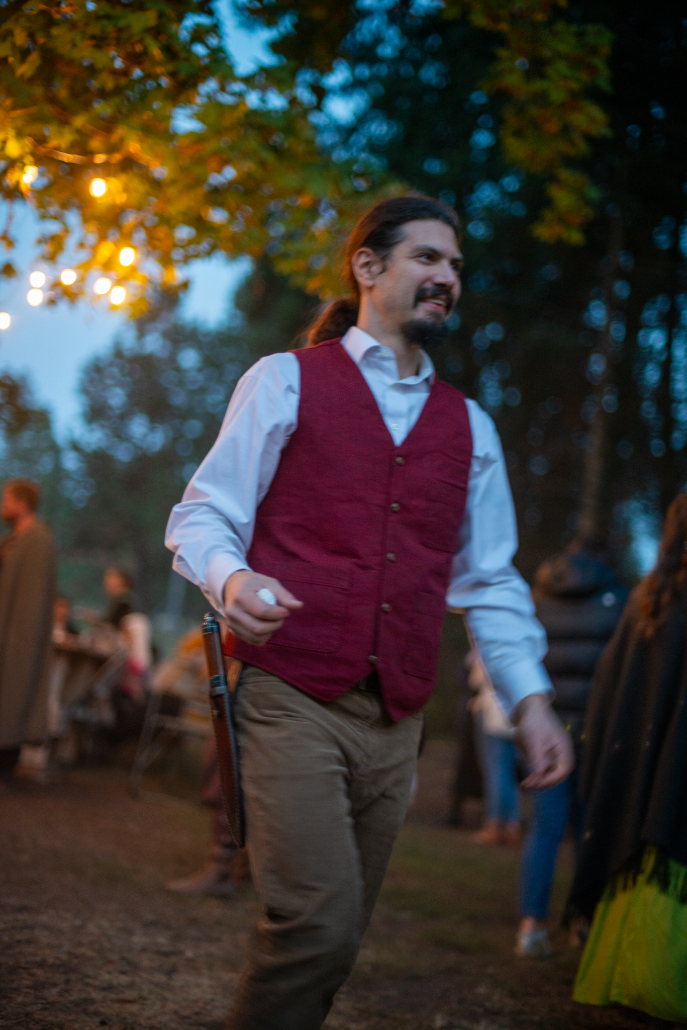 A smiling guest in a burgundy waistcoat walking beneath the lit party tree
